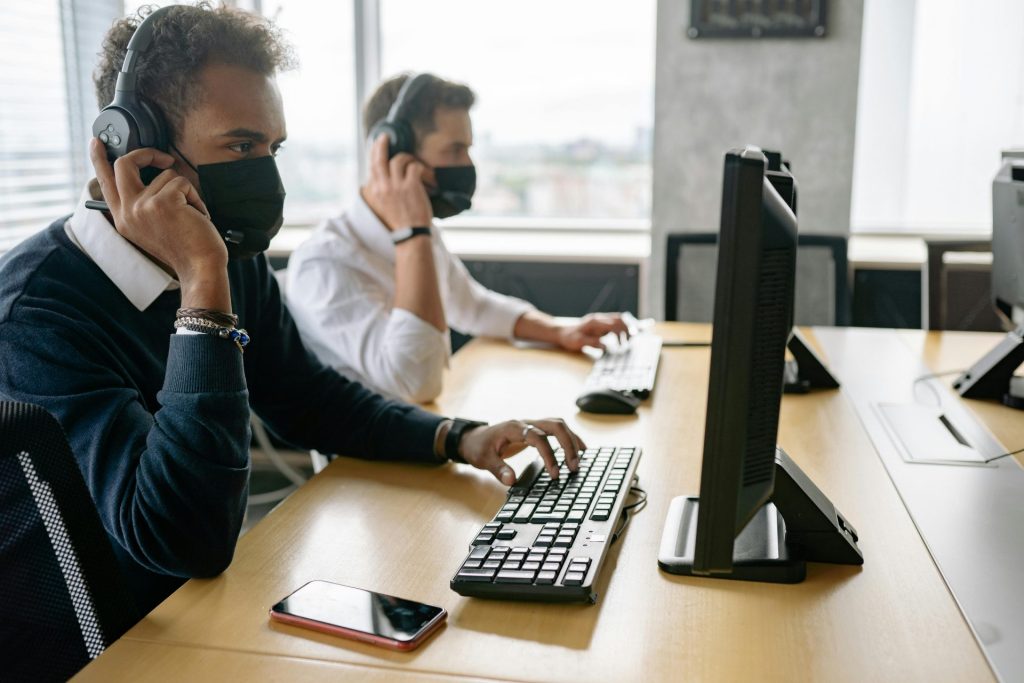 Two agents wearing face masks working on computers in a modern office.